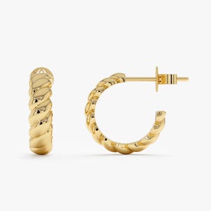 May include: A pair of gold-colored hoop earrings. Each earring has a twisted rope design. The earrings are displayed on a white background. The earrings have a post and butterfly clasp.