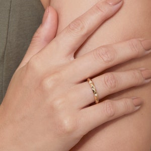 May include: A gold ring with a textured, triangular design. The ring is worn on a person's finger.