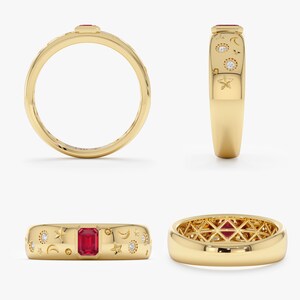 Op de afbeelding: Een gouden ring met een centrale smaragdgeslepen rode edelsteen, versierd met gegraveerde hemelse motieven zoals sterren en maansikkels, en kleine ingezette ronde witte stenen. De binnenkant van de band heeft een geometrisch rasterpatroon.
