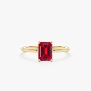 May include: A gold ring with a striking rectangular, red gemstone. The gemstone is held securely by four prongs. The band is a smooth, polished gold, offering a classic and elegant aesthetic. The ring's design is simple yet sophisticated.