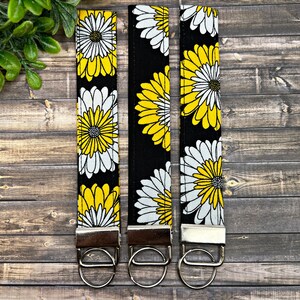 May include: Three black and white keychains with yellow daisy floral patterns and silver key rings.