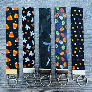 May include: Set of six Halloween-themed keychains with different patterns. The keychains are black with orange, white, and green accents. Each keychain has a metal ring.