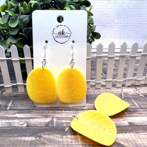 May include: Yellow potato chip shaped earrings with a textured surface. The earrings are hanging on a white card with the text "ak DESIGNS".