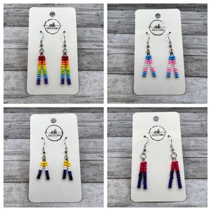 May include: Four pairs of beaded earrings on white cards with the text "ak designs". The earrings are in the colors of the rainbow, transgender, bisexual, and lesbian pride flags.