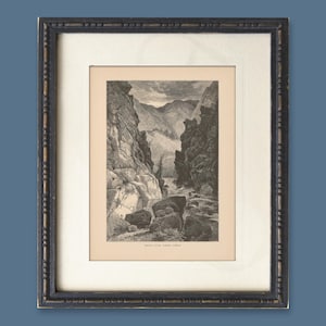 Puede incluir: Impresión en blanco y negro enmarcada de un paisaje de cañón. La impresión está dentro de un passe-partout blanco y un marco de madera oscuro y ornamentado. El cañón presenta acantilados rocosos, un río y montañas distantes. La impresión está etiquetada como "BRYCE CANYON, UTAH".