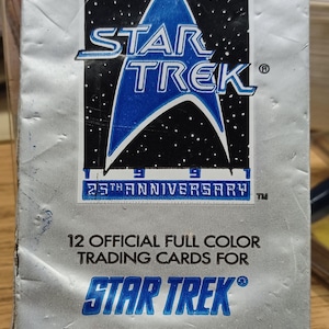 Może przedstawiać: Srebrny pakiet foliowy z kartami kolekcjonerskimi Star Trek. Pakiet zawiera ikoniczne logo Star Trek z niebiesko-czarną odznaką Gwiezdnej Floty. Tekst na opakowaniu brzmi: "12 Oficjalnych Kartek Kolekcjonerskich w Pełnym Kolorze do Star Trek Oryginalny Serial Telewizyjny 25-lecie".