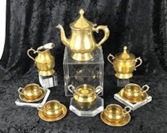 May include: A gold-toned tea set with a teapot, creamer, sugar bowl, and four cups and saucers. The set is arranged on a black velvet surface.