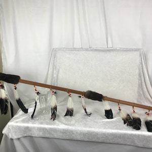 Puede incluir: Una lanza de madera con una punta de metal y plumas. La lanza está decorada con cuentas y piel.