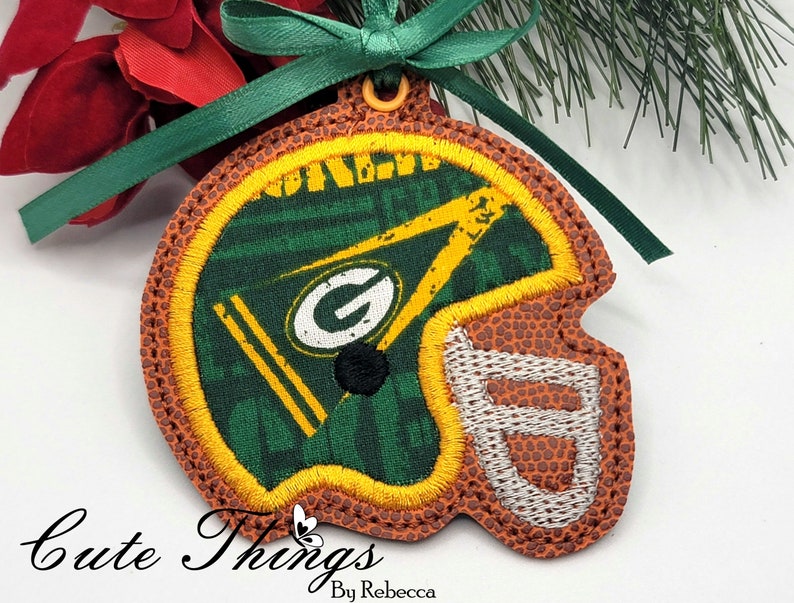 Op de afbeelding: Groen en gouden voetbalhelm ornament met een bruine lederen textuur. De helm is versierd met een groen en gouden patroon en een witte omtrek. Het ornament heeft een groen lint.