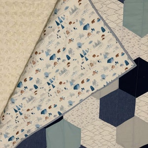 May include: A white and blue baby quilt with a geometric pattern of hexagons. The quilt is made of soft fabrics and features a woodland animal print on the back.