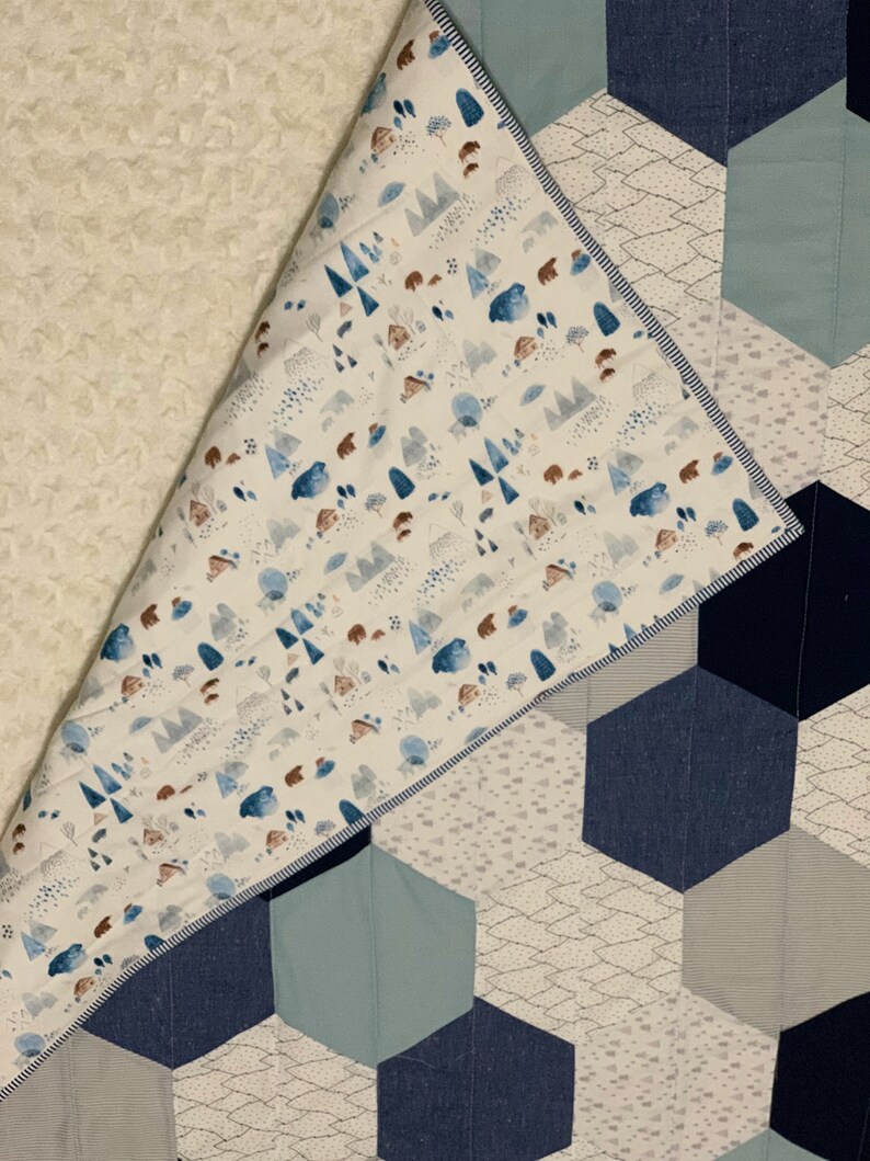 May include: A white and blue baby quilt with a geometric pattern of hexagons. The quilt is made of soft fabrics and features a woodland animal print on the back.