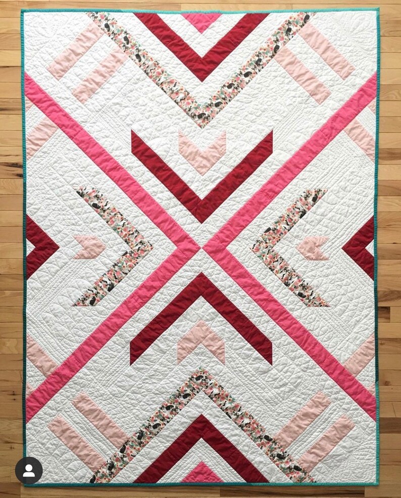 May include: A white quilt with a geometric pattern of pink, red, and floral fabric. The quilt is edged with a teal border.