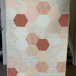 May include: A pink and red hexagonal quilt with a variety of patterns. The quilt is made of cotton fabric and has a white background.