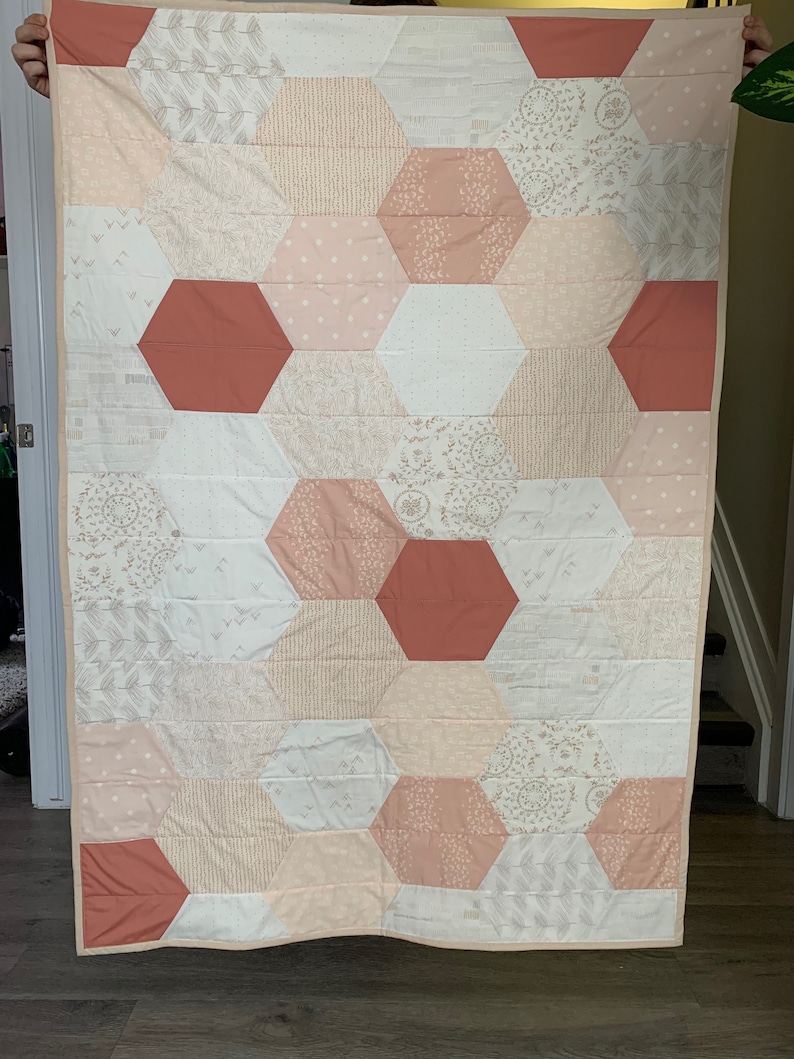 May include: A pink and red hexagonal quilt with a variety of patterns. The quilt is made of cotton fabric and has a white background.