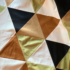 May include: A quilt made of fabric triangles in shades of brown, green, black, and white. The triangles are arranged in a repeating pattern.