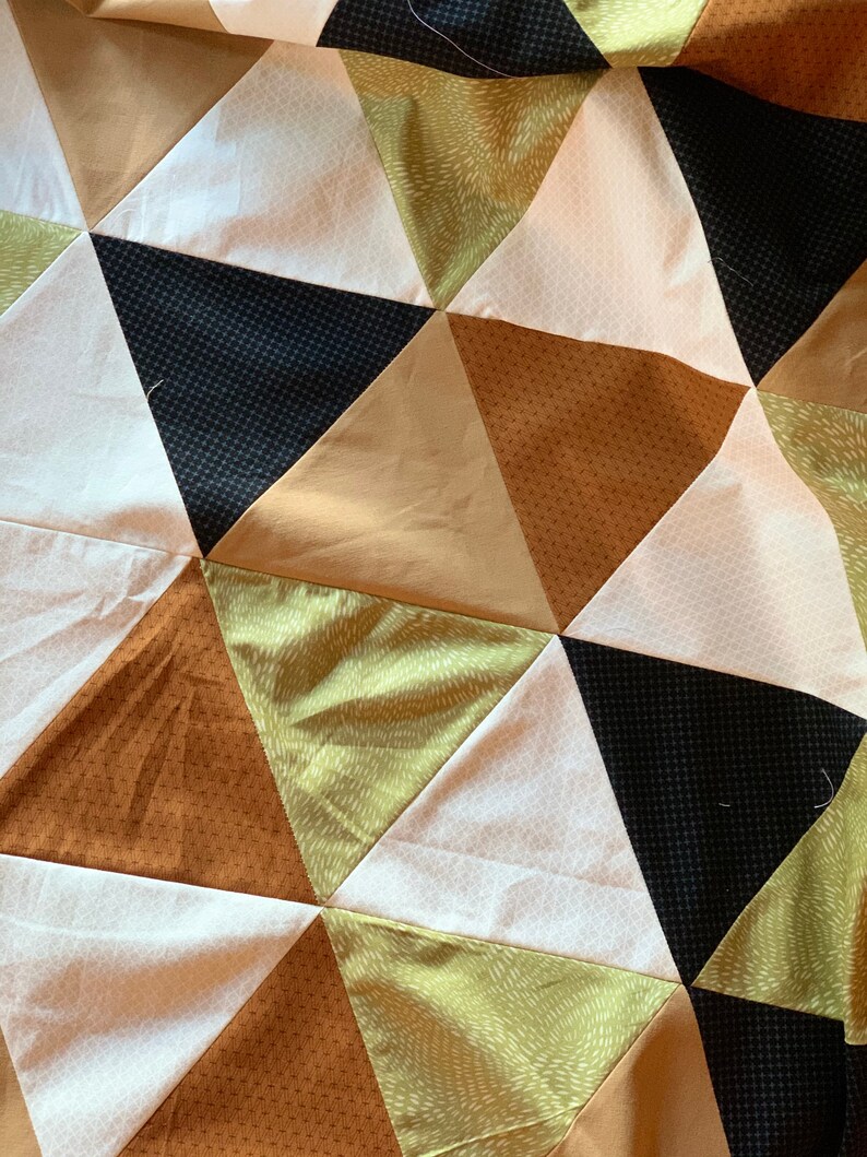 May include: A quilt made of fabric triangles in shades of brown, green, black, and white. The triangles are arranged in a repeating pattern.