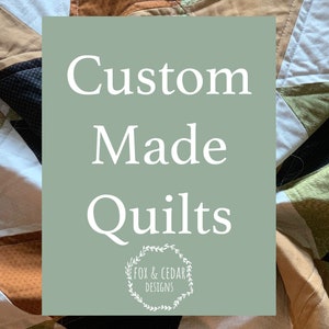 May include: A green and white sign with the text "Custom Made Quilts" and a logo that says "Fox & Cedar Designs". The sign is in front of a patchwork quilt with various colors and patterns.