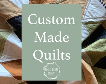 May include: A green and white sign with the text "Custom Made Quilts" and a logo that says "Fox & Cedar Designs". The sign is in front of a patchwork quilt with various colors and patterns.
