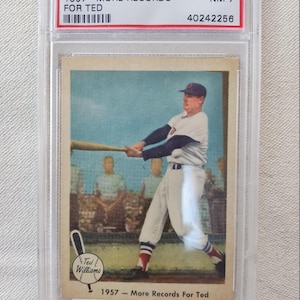 May include: A vintage baseball card of Ted Williams, encased in a protective holder. The card features a color image of Williams swinging a bat. Text on the card reads "1959 Fleer T. Williams 1957 - More Records For Ted".