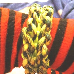 Puede incluir: Un brazalete de paracord tejido en verde y amarillo.
