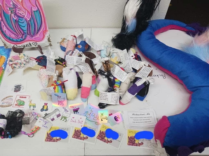 May include: A table top display of colorful handmade sock puppets with various designs and patterns. The puppets are arranged in rows and include a variety of colors, including pink, blue, green, and yellow. There are also several small cards with text on them, including "Back Dot" and "Welcome Home, Mia".