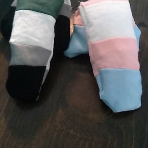 May include: Two fabric finger puppets, one with green, white, gray, and black stripes, and the other with white, pink, light blue, and dark blue stripes.