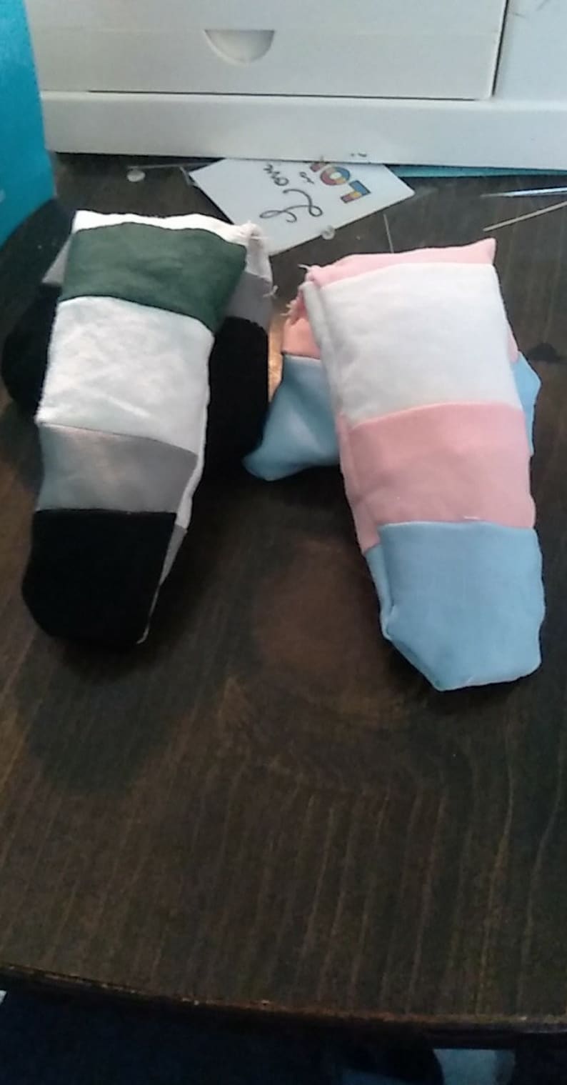 May include: Two fabric finger puppets, one with green, white, gray, and black stripes, and the other with white, pink, light blue, and dark blue stripes.