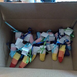 May include: A cardboard box filled with colorful fabric pouches tied with ribbons. The pouches are decorated with rainbow stripes and have small tags attached.