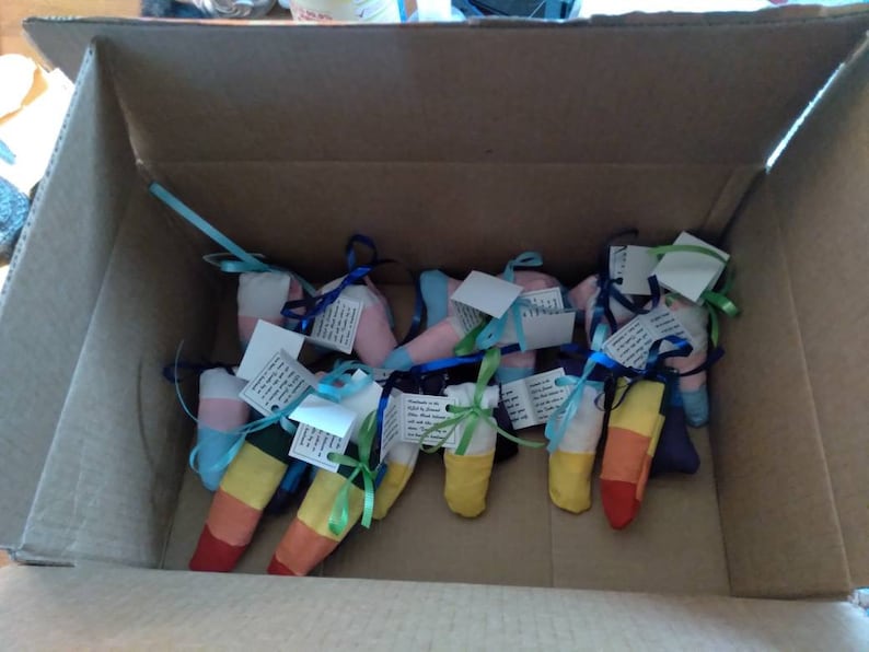 May include: A cardboard box filled with colorful fabric pouches tied with ribbons. The pouches are decorated with rainbow stripes and have small tags attached.