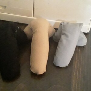 May include: Three fabric armrests in black, beige, and gray. The armrests are all the same size and shape, and they are lying on a wooden surface.