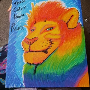Puede incluir: Una pintura colorida de la cabeza de un león con el texto "These Colors Don't Run." La melena del león es naranja, amarilla y roja, y el fondo es azul y verde.