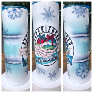 May include: A white and blue insulated tumbler with a winter theme. The tumbler features snowflakes and the words "Experienced Ball Handler" with a graphic of skeleton hands holding ornaments. The lid is blue.