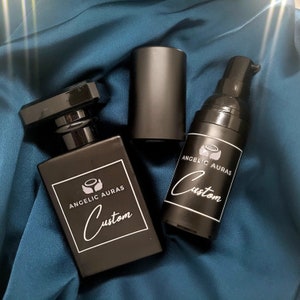 Puede incluir: Tres botellas negras con etiquetas blancas. Las etiquetas tienen el texto "Angelic Auras Custom" y un peque&ntilde;o dise&ntilde;o de alas de &aacute;ngel.