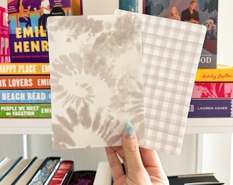 May include: Two decorative cards, one with a white and grey tie-dye pattern and the other with a white and grey gingham pattern. The cards are held in a hand.