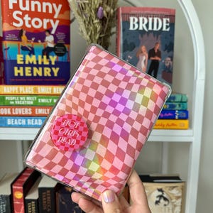 May include: A pink and white checkered book cover with a holographic effect. The cover has a pink button with the text "Hot Girls Read" on it.