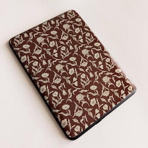 May include: A rectangular electronic reader device featuring a dark brown cover with a repeating pattern of light beige flowers, stems, and leaves. The device has rounded corners and a smooth, glossy finish across the entire front surface.