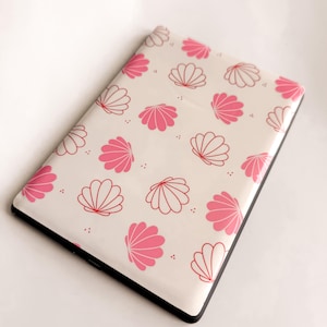 May include: A rectangular, off-white case with a black border, adorned with a pattern of pink and red seashell illustrations. The design features alternating solid pink and outlined red shells, creating a decorative and eye-catching aesthetic.