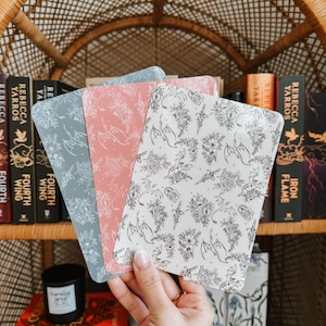 以下が含まれることがあります： 花柄とドラゴン柄の装飾的なしおり3つ。しおりはピンク、ブルー、ホワイトの色合いです。