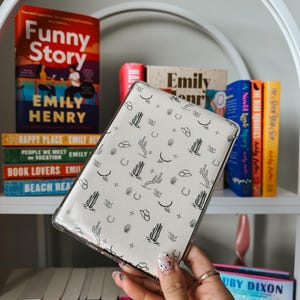 May include: A white phone case with a black and white pattern of cacti, stars, horseshoes, and cowboy hats.