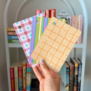 May include: Three rectangular plastic cards with rounded corners and a single hole punch. The first card features a pink and blue plaid pattern with stars. The second has vertical green, blue, and purple stripes. The third is orange with a grid.
