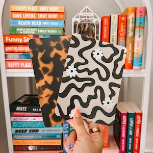 May include: Two decorative rectangular cards. One features a tortoiseshell pattern in shades of brown and black. The other has a beige background with black wavy lines and white daisy accents. Bookshelves are in the background.