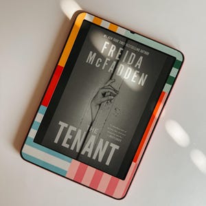 Puede incluir: Un lector electrónico con una funda estampada. La pantalla muestra la portada del libro "The Tenant" de Freida McFadden. La funda presenta rayas en rojo, naranja, rosa, azul y verde.