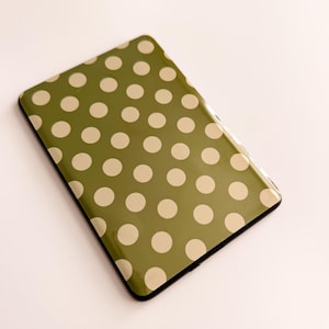 May include: A rectangular electronic tablet device featuring a smooth, glossy olive green exterior surface decorated with a repeating pattern of light cream-colored polka dots arranged in uniform horizontal and vertical rows.