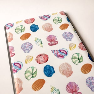 May include: A white background with a repeating pattern of colorful seashells. The seashells are in various shapes and sizes, including scallop, conch, and clam shells. The shells are painted in shades of pink, blue, green, orange, and purple.