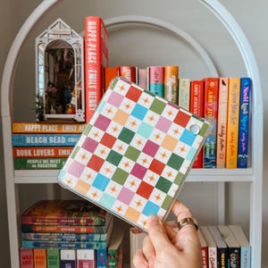 May include: A clear tablet case with a colourful geometric pattern of squares and stars. The case is held in front of a white bookshelf filled with books of various colours and titles.