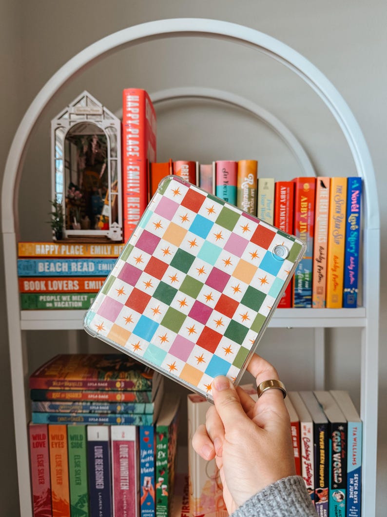 May include: A clear tablet case with a colourful geometric pattern of squares and stars. The case is held in front of a white bookshelf filled with books of various colours and titles.