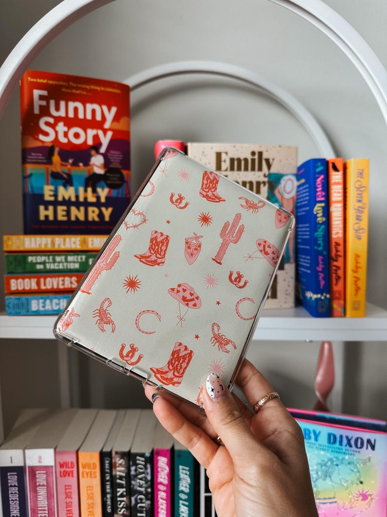 May include: A clear phone case with a light green background and a repeating pattern of red cowboy boots, cacti, scorpions, and stars. The case is being held in a hand.