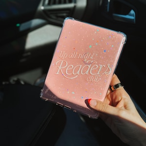 以下が含まれることがあります： キラキラ光るピンクの携帯電話ケースに、白い文字で「Up all night Readers club」と書かれています。