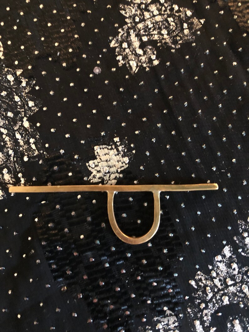 May include: A gold-coloured metal ring with a simple, minimalist design. The ring features a straight bar with a rounded loop at the centre.