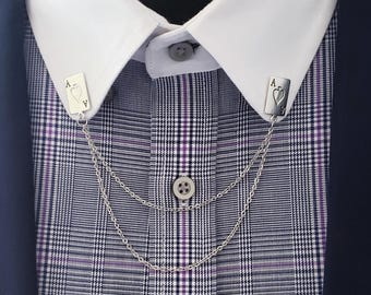 May include: A silver collar bar with Ace of Hearts card design, connecting the collar points of a white dress shirt. The shirt is under a navy blue blazer, with a purple and black plaid pattern. The collar bar has a chain.